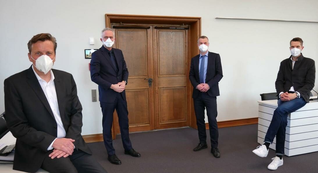 Das Bild zeigt vier Männer die mit Abstand nebeneinander stehen und einen Mundschutz tragen.