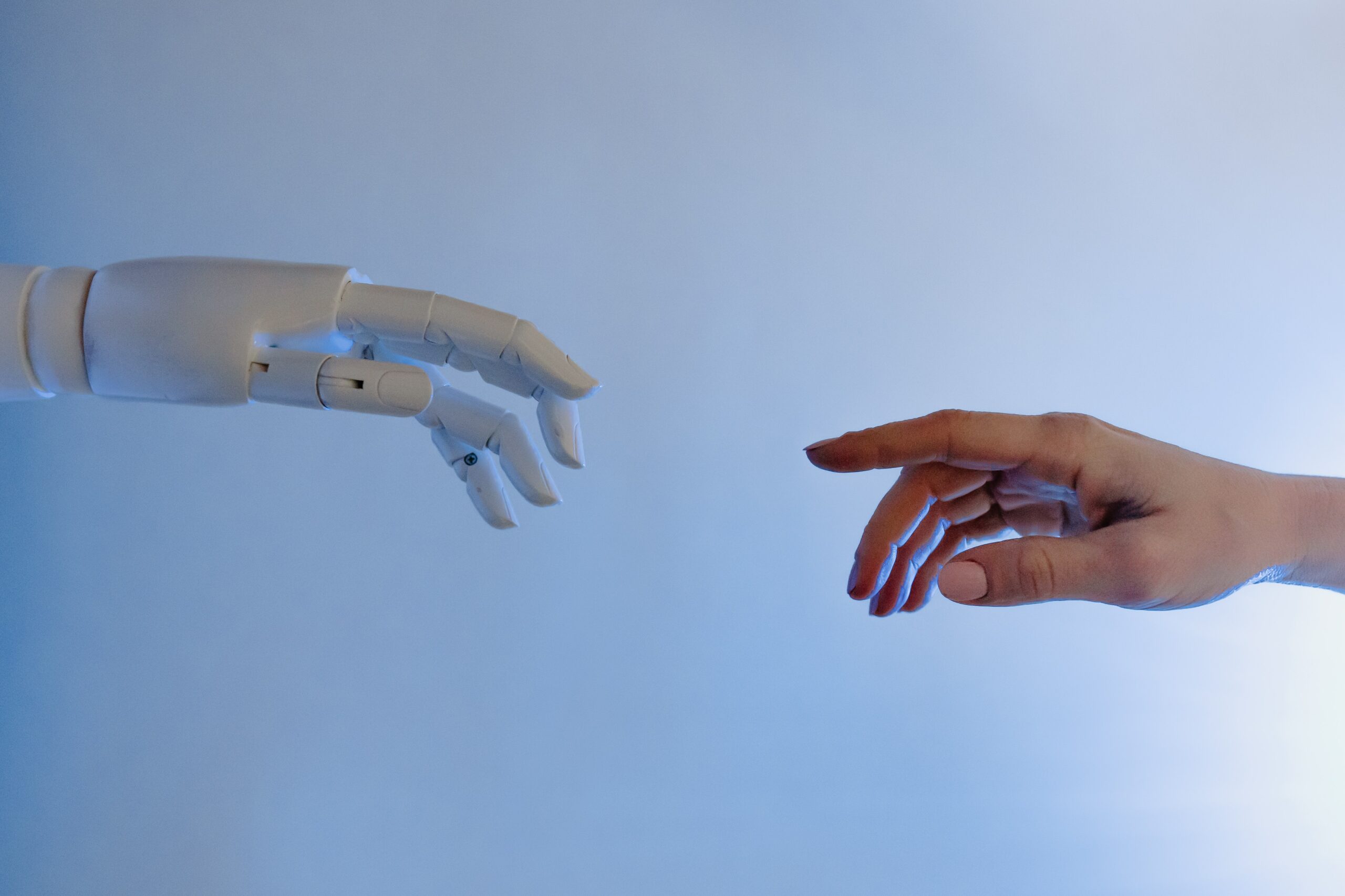 Die Hand eines Roboters und die Hand eines Menschen die aufeinander zeigen.